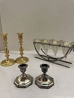 Photo showing two tall gold-colored Baldwin candlestick holders, two smaller silver-plated EP Zinc 806 candlestick holders, and a glass candle holder in a metal frame.