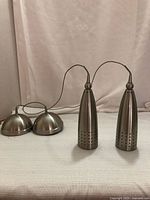 Two silver metal pendulum lights placed upright side by side with their wiring and metal canopy bases visible in the background.