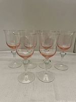 Six clear wine glasses with rose tint on base and rim arranged in two rows on white surface.