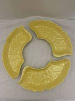 Three yellow leaf-shaped pottery serving dishes arranged in a circle, showing the leaf vein details and curved shape.