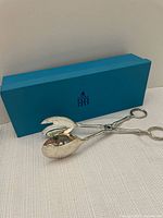 Pair of silver plated salad/pastry tongs with a blue Birks box in the background, shown from an angled top view.