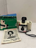 Photo of Polaroid Swinger Model 20 land camera with original box and instruction manual, showing overall condition and contents of the lot.