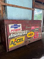 Closed vintage red metal toolbox with various automotive brand stickers on exterior