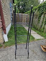 Front view of black metal stand with three foldable shelves and gold ball finials on each corner post