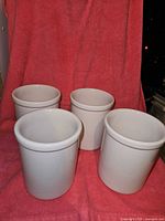 Photo showing all four white ceramic jars with rolled rims, placed on red cloth background.