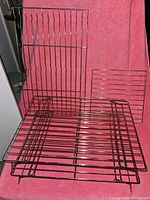 Four metal cooling racks on a pink fabric background. Two racks are upright and appear stackable and foldable with raised legs, two racks lie flat and are regular cooling racks.