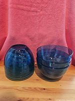 Six blue translucent plastic bowls stacked, showing ribbed textured bases and rounded shape.