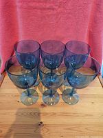 Six blue translucent plastic wine glasses arranged in two rows of three with a red cloth background and wooden surface.