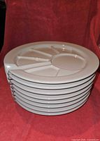 Stack of 8 white ceramic fondue plates showing the side profile and thickness.