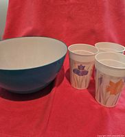 Photo showing the blue plastic salad serving bowl and three white plastic cups with flower designs on a red background.