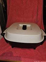 Electric Dutch oven with white lid and black handle on top, body black with side handles.