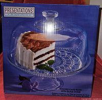 Box front showing glass footed cake plate with dome, displaying a cake and floral decoration as example use.