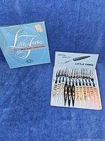 Photo of a set of 12 appetizer forks in original box, showing handles in white, black, cream, blue, and pink with floral designs.