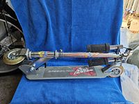 Folded metal scooter placed horizontally showing the deck with 'Speedway' branding and flame graphics on the metal frame.