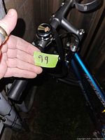 Close-up of bike handlebars showing the bell and hand grips as well as a hand holding a green label with number 99.