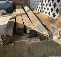 Posts laid side-by-side on concrete showing weathered ends, cracks and paint