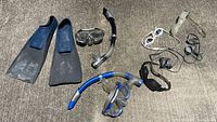 All 10 items laid out on concrete: fins, masks, snorkels, goggles, straps