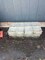 Lot of 24 glass bricks stacked outdoors against a wall, showing size and quantity.