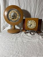 Photo showing two clocks side by side: round wooden mechanical clock and wooden case electric United clock with power cord.