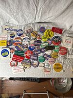 Top-down image of approximately 40 diverse political campaign buttons and pins laid out on a white fabric background, featuring various colors, slogans, and candidate names mostly from Ohio elections, including presidential campaigns from the 60s to 90s.