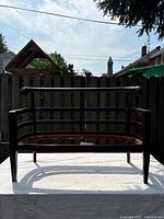 Front view of antique wooden bench frame showing horizontal slats and armrests, on white cloth.