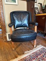 Front view of an antique armchair with a solid wood frame and black leather upholstery showing cracking and wear.
