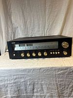 Front and top view of Audio Reflex AR-825 stereo receiver with knobs and AM/FM dial visible, unit placed on a fabric-covered surface with neutral background.