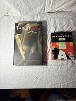 Front view of 'Tarot Sutra' book and 'The Observation Deck' cards side by side on white fabric.