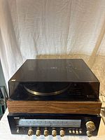 Closed view of BSR vintage turntable on top of audio receiver with tinted dust cover, wood grain base, and black control panel.