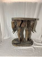 Front view of the carved elephant side table showing the three elephants under the top surface and oval base.