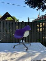 Left profile view of purple upholstered fiberglass shell armchair on cast aluminum swivel base with casters
