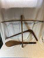 Three wooden martial arts props displayed against a white fabric backdrop including a crossbow, curved boomerang-like weapon, and club.