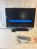 Front view of Toshiba small TV monitor showing screen with 'No video signal' message and oval base, remote and manual in bag in front.
