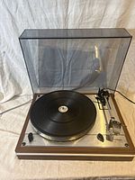 Front quarter view of Thorens TD 165 turntable with hinged clear dust cover lowered showing platter, plinth, tonearm and power cord