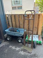 Metal wagon with four tires, some damaged, and cargo dolly against fenced background