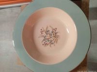 Photo showing the full front side of the antique ceramic plate with a green rim and floral design in the center.