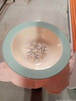 Round plate with light blue rim and floral decoration on cream base placed on table covered with pink cloth