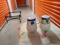 Photo of two antique salt and pepper shakers on a cloth with a storage unit background.