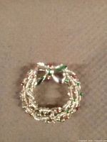 Front view of a gold-tone Christmas wreath brooch with green and red rhinestones and bow detail on a fabric background.