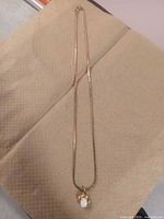 Gold-tone chain necklace laid out flat on a beige fabric surface with oval pendant attached at center.