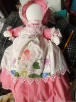 Front view of the doll showing the pink dress and white apron with floral embroidery