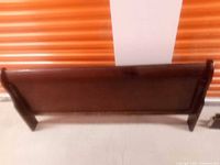 Photo of the footboard of the oak bed frame showing its dark stain and curved design.