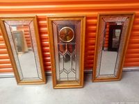 Three-piece set includes one glass wall clock with wood frame flanked by two matching framed mirrors.
