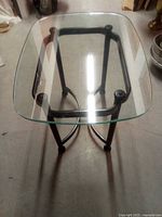 Top angled view of the rectangular glass end table highlighting the transparent tempered glass surface and black curved metal legs with cross support.