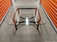 Top-view photo of the square glass coffee table showing the transparent glass top and metal base structure with four tubular legs and a central support design.