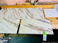 Four varying rectangular white marble slabs with brown and beige veining on a wooden surface showing thickness and polish.