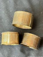 Three sterling silver napkin rings on dark cloth background, two with hammered texture and one lined Christofle example