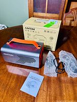 Photo showing the AIMTOM portable generator power station, original box, instruction manual, and charging cables on a wood surface.