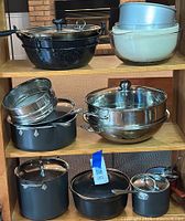 Full view of shelves holding various cookware including All-Clad Ltd pieces and other items such as enamel roasting pan, mixing bowls, stainless steel bowls and steamer insert.