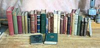 Photo showing full collection of 23 decorative antique books with various colors and sizes lined up on a wooden surface.
